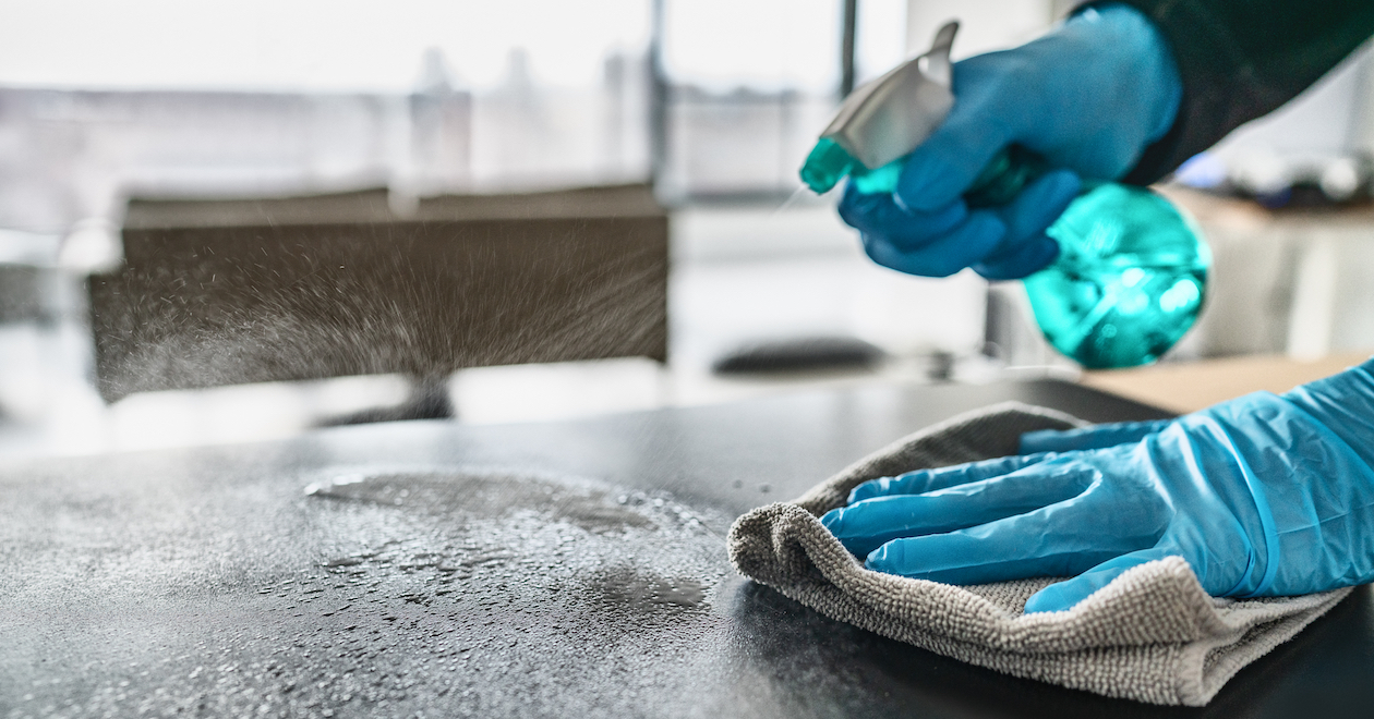 Hands cleaning a surface with spray and a cloth