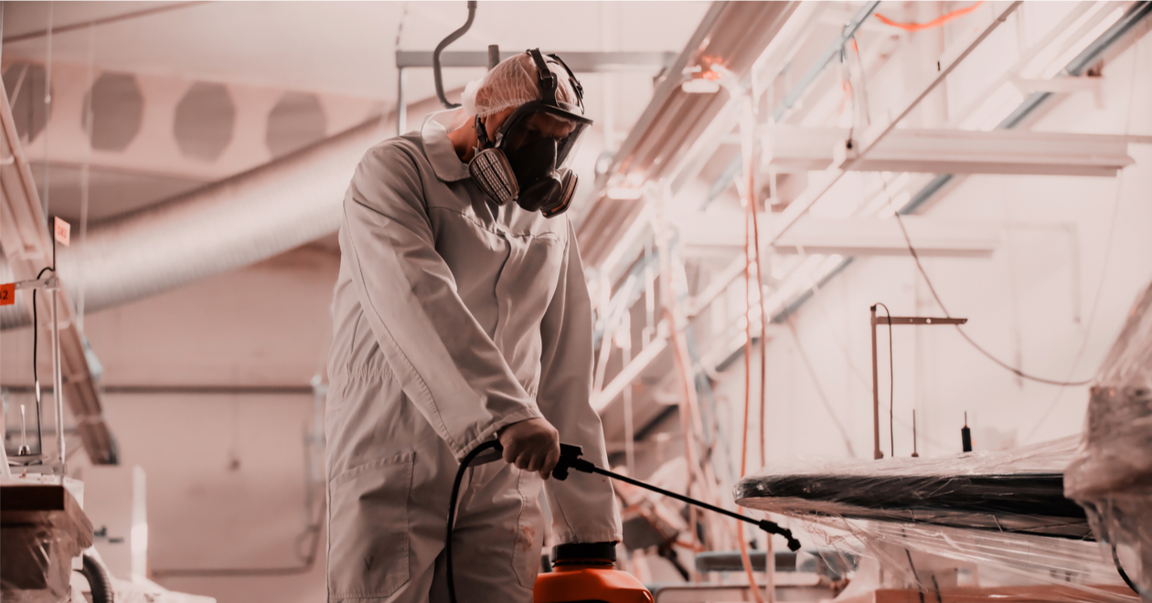 A person in protective clothing spraying a workplace with disinfectant