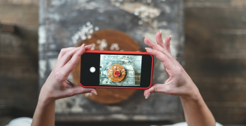 Cropped view of young adult food stylist using modern smartphone, making content for social media blog.