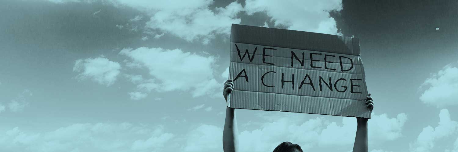 A person holding aloft a cardboard sign that reads 'we need a change' 